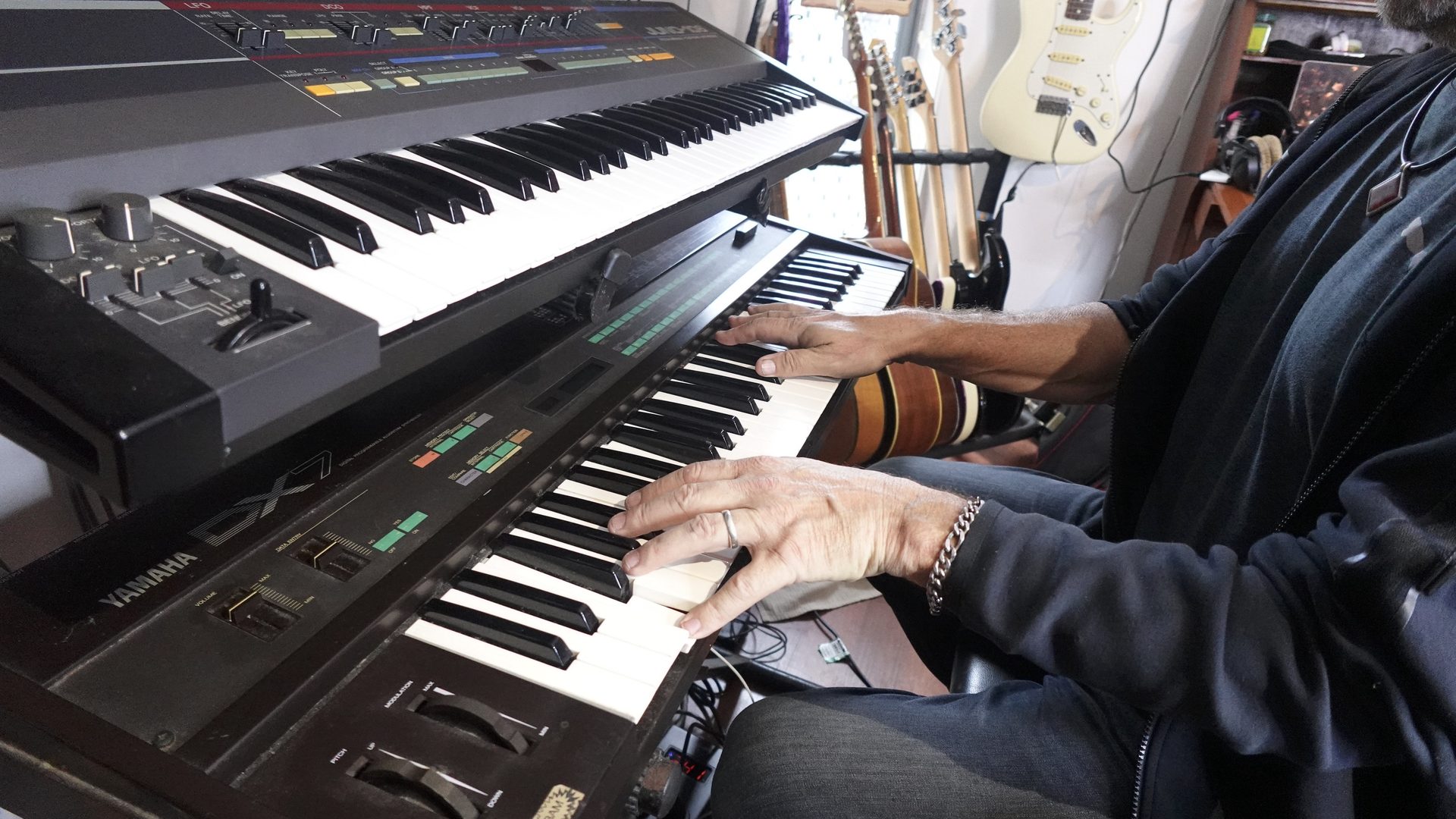 A musician playing keys in a home studio surrounded by guitars